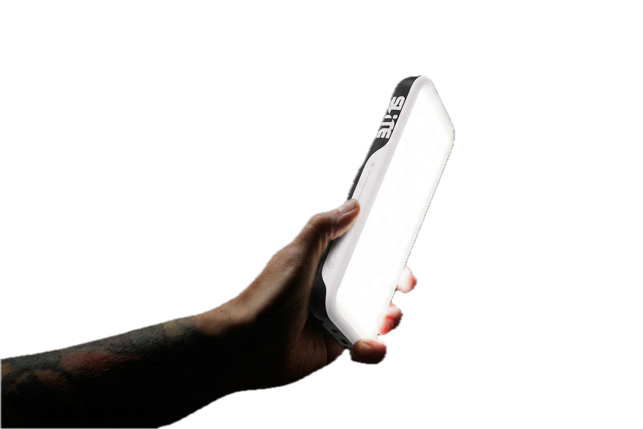 A tattooed forearm out of the black holding a SLITE.one, its lit face turned to camera